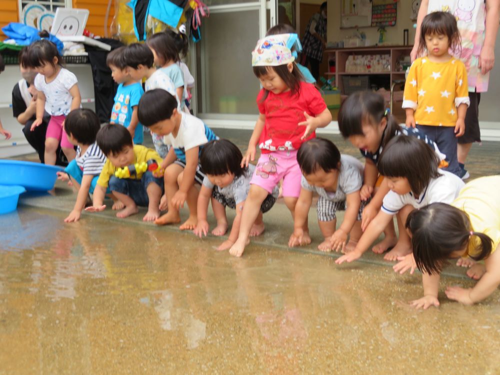 子どもたちも我慢しきれず・・・ひとりふたりと、おみずをパシャパシャ💦

「入っちゃおうかな～」足をそ～～っとだしたら・・・
『今日は寒いからだめ～』と先生にみつかっちゃった！
残念・・・

みんな手をのばして、水たまりにタッチ～！
それだけでもたのしそう。だけど・・・
早く思う存分水遊びしたいね。
「おひさま～でておいで～～」

