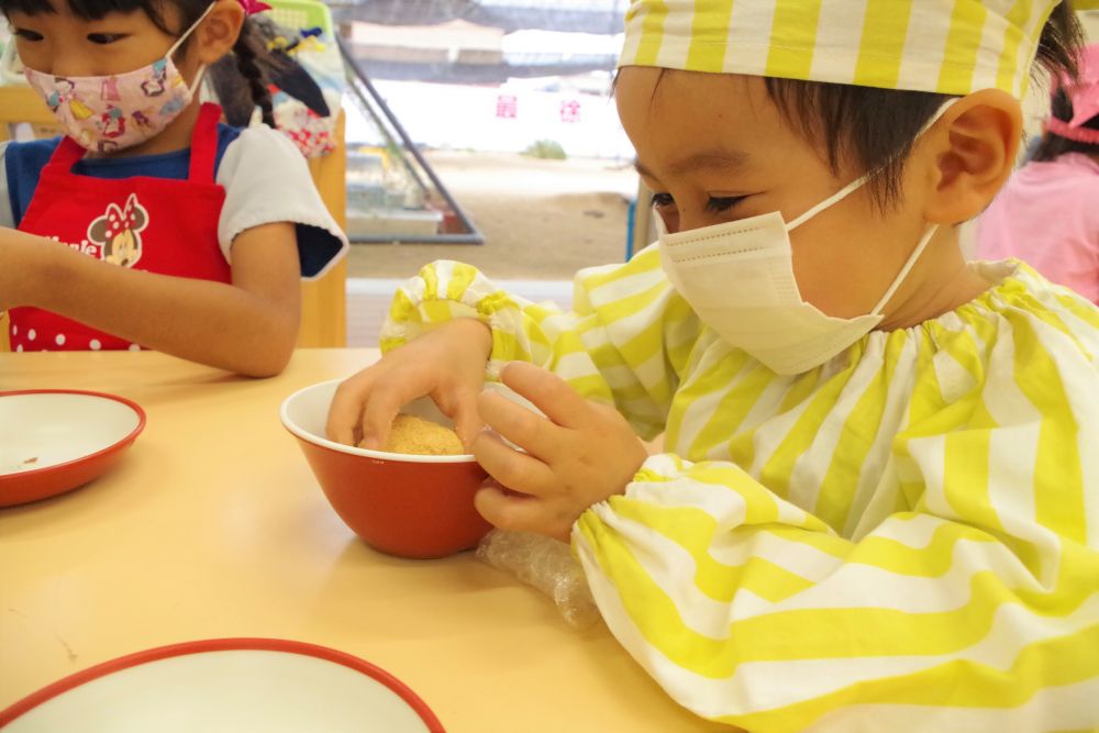 まずは、ラップに包んだご飯を指でしっかりもんでつぶします。
このときの感触が楽しいようで、
「おぉ～むにゅってする～」
「つぶしたら匂いがいっぱいしてくるよ」
と、色んな感想が聞こえてきます。

ご飯をつぶした後は、ラップの上で平らにのばします。
「次はあんこよね？」
「中に入れるんでしょ？」
と、あんこを包むのを楽しみにしている様子の子ども達♪