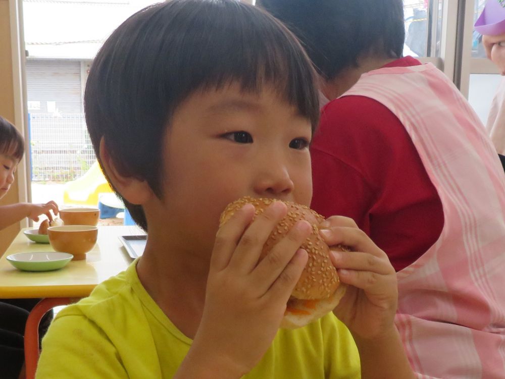 今日は９月の誕生日会♡
献立は【ハンバーガー】です。

給食の時間になるとお腹がすいてきたのか、給食室を覗きに来る子がちらほら・・・
「ハンバーガーだ！！」と嬉しそうな声が聞こえました♡

みんな興味津々でハンバーガーから食べ始めます。
リス組さんは「大きいね～！」としっかり両手で持って大きなお口でパクッ。