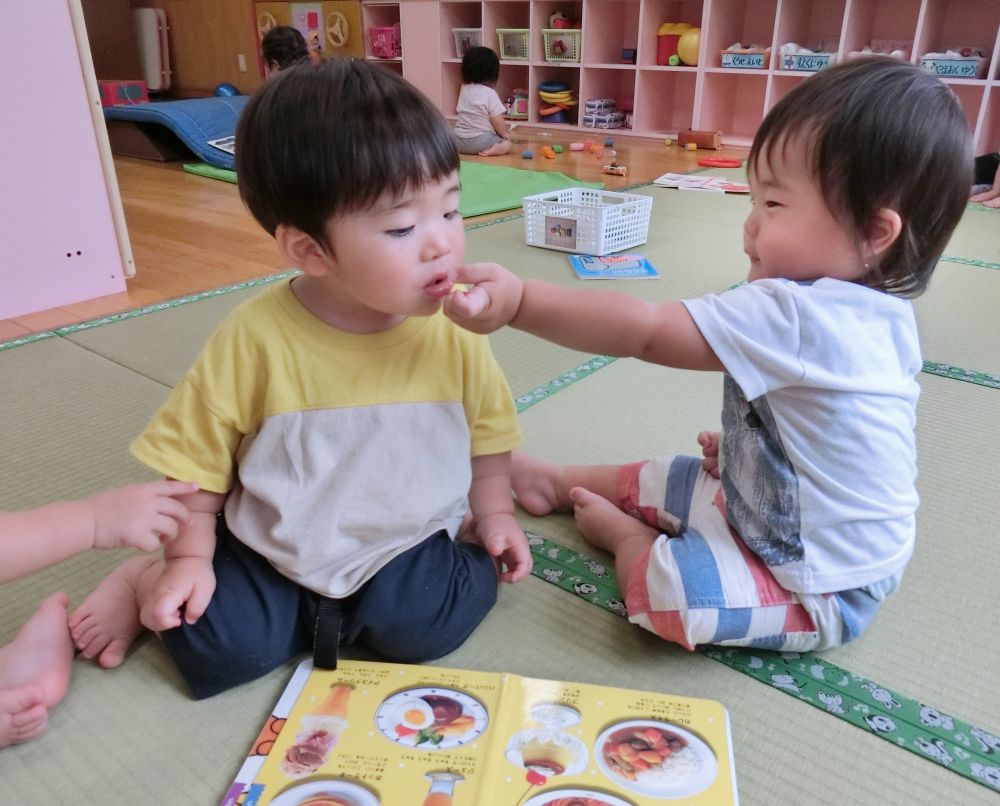 食べ物の絵本を見ながら、お互いのお口に「あ~ん」と食べさせてあげようとしている、かわいい姿を発見!
月齢の大きなウサギぐみさんはお友達の存在を認識して、一緒に遊ぶ姿が見られるようになってきました。言葉はまだなくても、しっかり気持ちは通じ合っている。
かわいい姿にほっこりしながらも、こういうやりとりができる環境作りを心がけていきたいと思う一場面です。