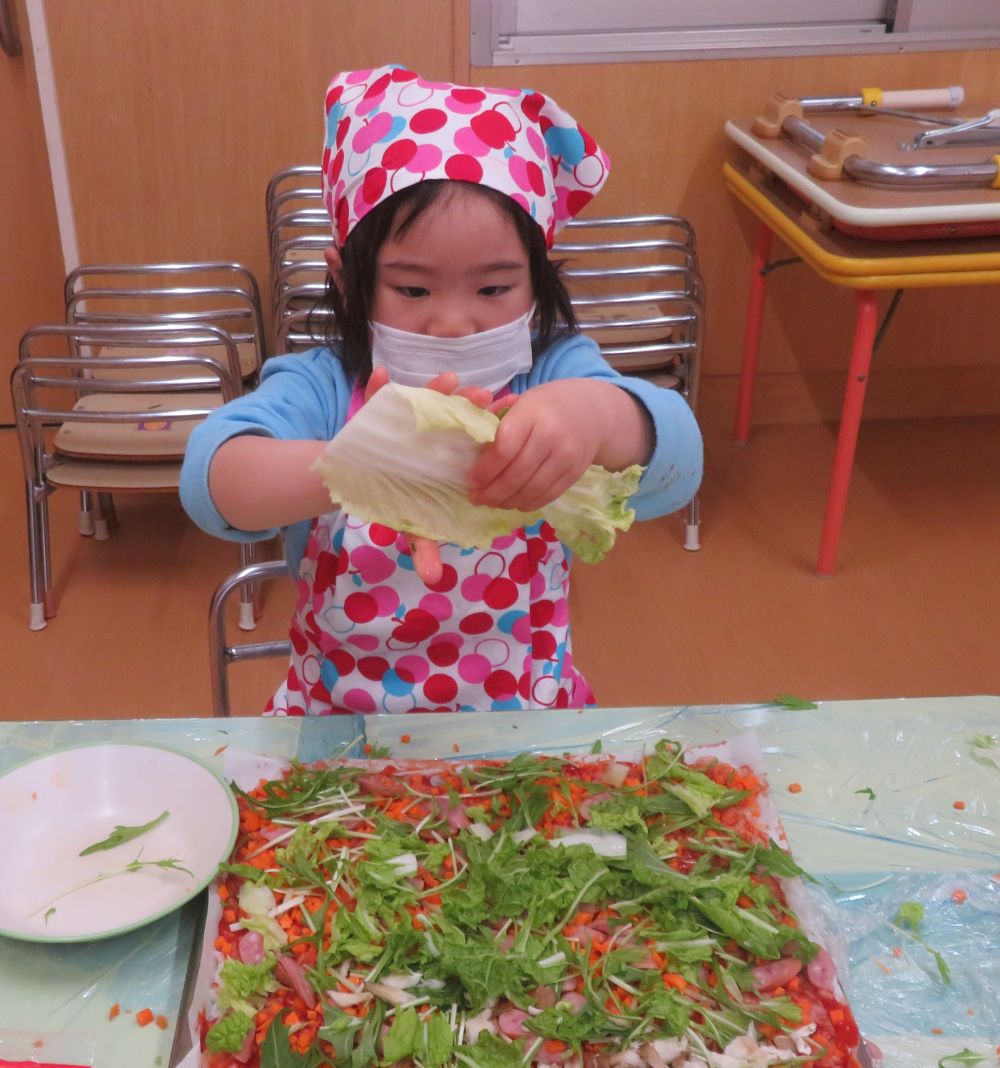 今日はリス組さんのクッキングで、おやつの【冬野菜のライスピザ】を作ります。
朝から「今日はピザを作るんだよ♪」と楽しみにしており、給食中もそわそわ・・・。
早く作りたいね！

昼寝から起きると、すぐにクッキングの準備に取りかかります。
エプロンを着けて、手をしっかり洗って・・・。
まずは、冬野菜が何があるか考えました。
今回は白菜、人参、水菜、えりんぎ、まいたけを使います。
ごはんの上に小さく切った野菜をのせていきます。
「ウサギ組さんも食べるから小さくしようね」