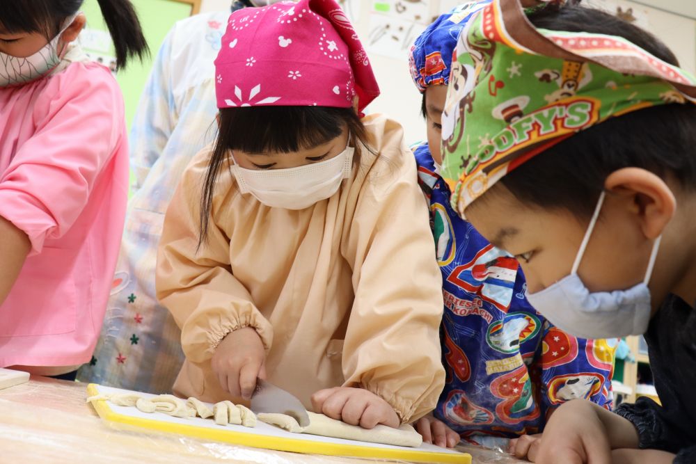 薄くのばしたら、３つに折りたたみ、いよいよ切る作業へ・・・。
包丁を使うのが初めての子も多かったですが、
「やりたい、やりたい」と意欲的な子ども達。
「左手はネコさんの手にするんよ」と手の添え方を知っている子が友達に教えてあげる場面も見られました。
包丁に慣れている子も、恐る恐るの子も、みんな真剣な表情で切っています。
一本切り終わるごとに「ふ～」と大きく息を吐き、
「何かわからんけど、切るとき息止めちゃう」と言う子もいましたよ。
必死になるあまり、呼吸を忘れる・・・真剣さが伝わります。