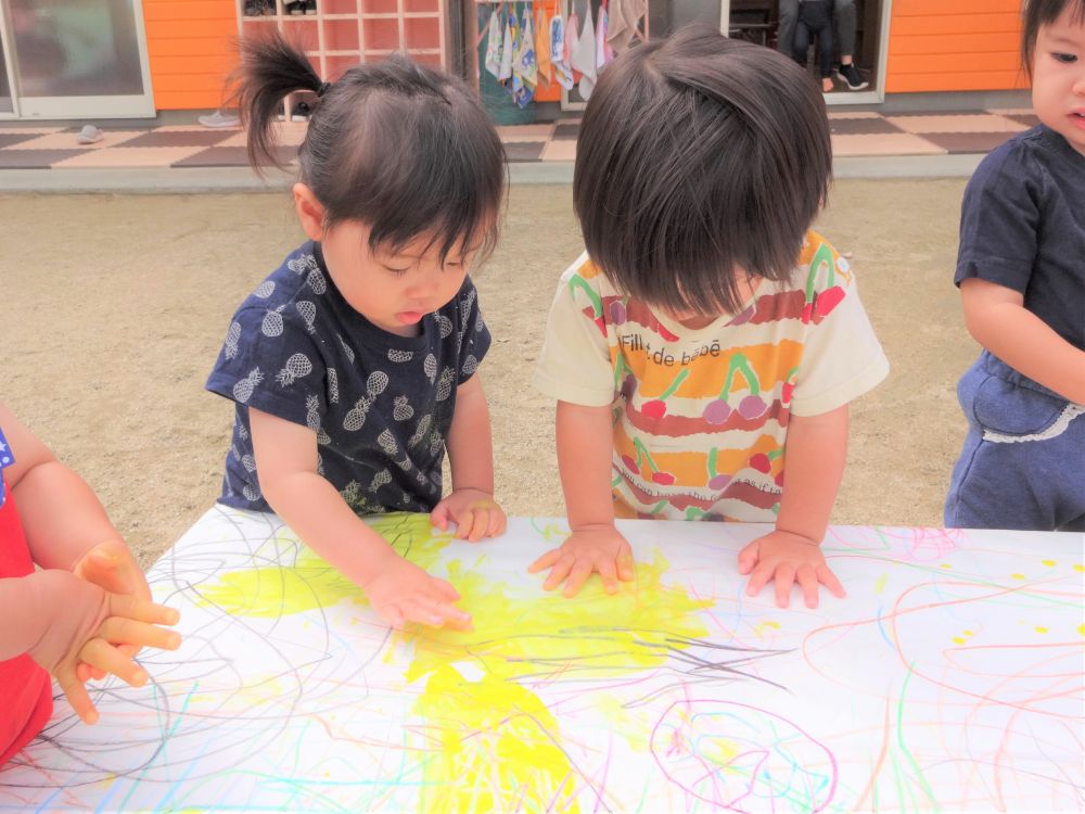 園庭に紙が貼ってあるテーブルを発見！
なんだなんだとヒヨコ組さん・・・
興味津々です♡



♪どんな色が好き～♪　歌いながら紙の上に絵の具をぽっとん…

すると・・・
Sちゃんが手のひらいっぱいに黄色の絵の具をつけて描き始めました
