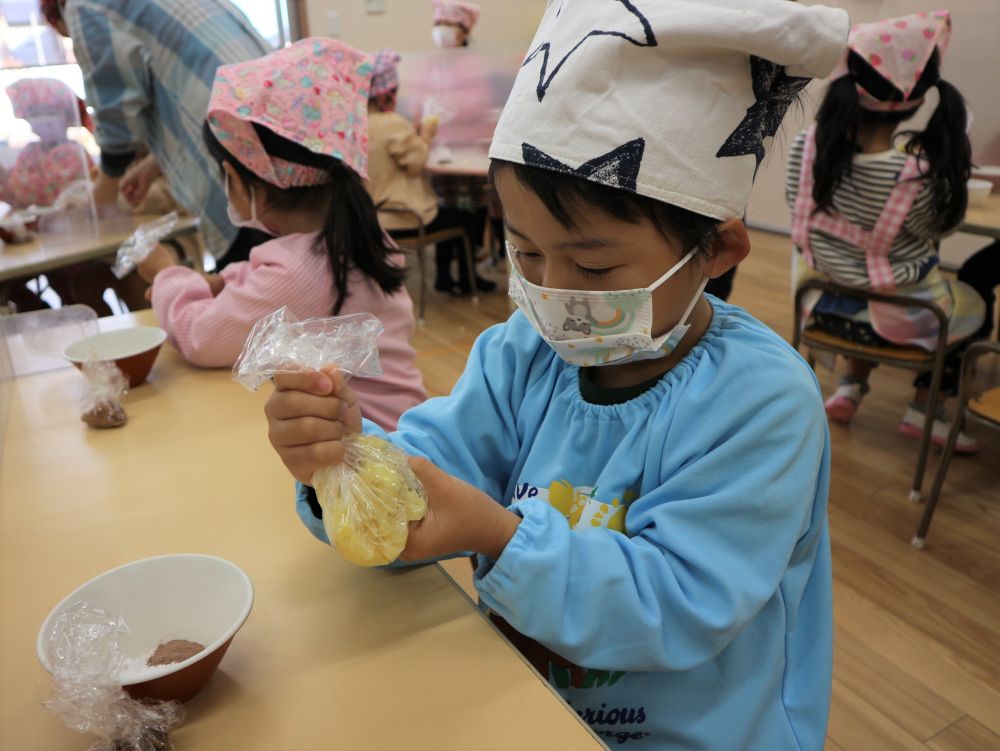 【１２月２０日】
ゾウ組さんが、クリスマスのお菓子作りに挑戦です☆
｢さつまいもde松ぼっくり｣っていうお菓子を作るよ、と伝えると
聞き慣れない名前に、みんなハテナ顔・・・（笑）
どんなものか想像できないけど、作ってみよう！と、クッキングスタートです♡

使う材料の確認をした後は、まずは松ぼっくりの土台となる、スイートポテト作りから。
茹でたさつまいもを袋に入れ、自分の指でつぶしていきます。
「あったか～い！ やわらかいからすぐつぶせるねぇ」
「つぶしたら、おいもの匂いがしてきたー」
それぞれ感じたことを伝え合いながら、作る工程を楽しみます♡