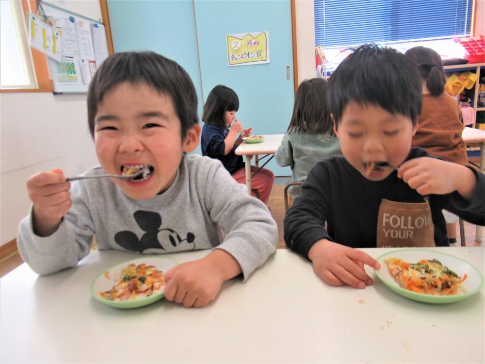 野菜をのせ、みんながのせたくてしょうがなかったウィンナーをのせ、最後にチーズをトッピング♪
具がてんこ盛りのライスピザ、焼き上がりが楽しみだね。

給食先生に預けて、待つこと15分・・・
焼きたてのピザが届きました！
「できた～！！」
「何か茶色くなっとる～♪」と、歓声が上がります。

グループの人数分に切り分け、できたてを「いただきます！」
「これ、私がちぎったまいたけ！」
「ウィンナーみっけ！」
と、具を確認しながら食べています。

野菜が苦手な子も、自分たちで作ったピザは完食♪
簡単にできるので、ご家庭でもぜひ、お休みの日のおやつにいかがですか？