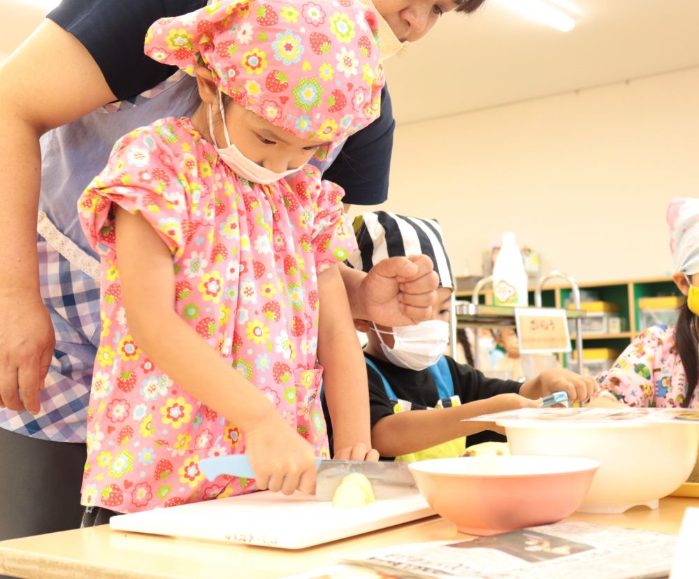 Ｋちゃん上手に包丁を使ってカットしています
自分でできることは自分で！！

しかし、保育者は心配で心配で・・・
後ろで見守る真由美先生の方が肩に力が入っています