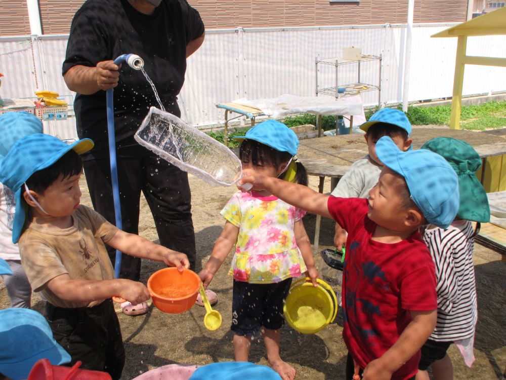 いよいよ子どもたちが楽しみにしていた水遊びの季節がやってきました！
今日は日差しが暑く、絶好の水遊び日和☆
クマ組の子どもたちはどんな風に遊ぶのかな？
ワクワクしながら、いざ園庭へ！

先生がホースでタライに水を入れようとすると

「お水ちょうだい！！」
「こっちにも入れて～！」

さっそく水の争奪戦！

