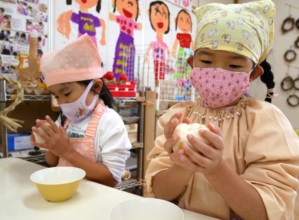 給食前の時間、炊きたてのアツアツを、さっそく握ります♡
一人分のご飯を、上手にラップにくるみ、にこにこ顔で「ぎゅっ」と持った子ども達。
「あっつ！！」
思ったよりご飯が温かかったようで、友達同士、顔を見合わせてビックリしたり、笑い合ったり・・・。それだけで何だか楽しい時間♡
「めっちゃあついねぇ～」
と言いながら、左右の手で交互に持ったりはなしたり・・・
ほどよく冷めたら、改めて両手で「ぎゅっ♡」