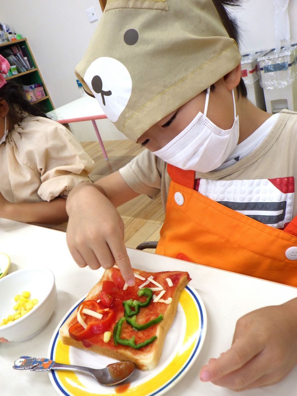 ケチャップをぬったら、あとは夏野菜とチーズをトッピングするだけ♡
四角いパンのキャンバスに、子どもたちの自由な発想が彩られていきます。

Tくんが自分のパンを見つめ、嬉しそうにしていたので「お、きれいにできたね！」と言うと
「このピーマンが鳥でね、こっちはちょうちょ」と教えてくれました。
湾曲したピーマンで、鳥が羽ばたく様子を表しているようです♡