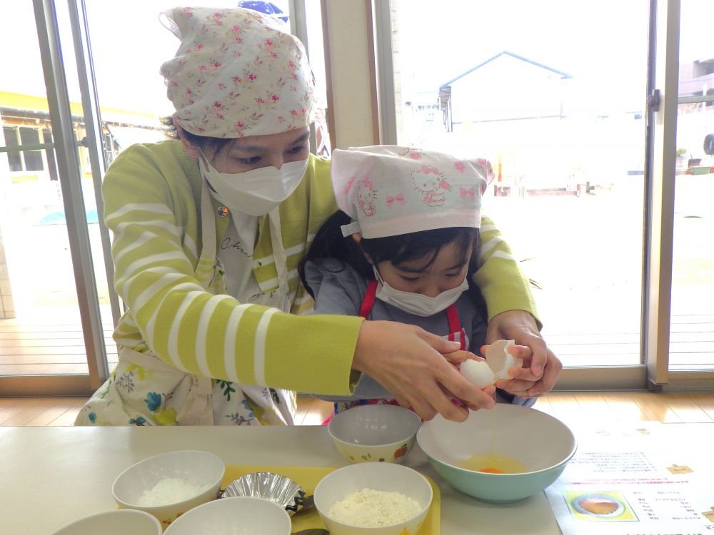 グループの材料が集まったら、今度は一人分ずつに分ける作業。
はかりを使い、必要な量を取り分けます。
親子３人の顔がひっつくくらい寄り添って計量する姿がほほえましたったです♡
「こぼれないように、そ～っとね」と慎重に、少しずつ量ります。
慣れない道具でも、おうちの人となら楽しんで使いこなしていますね♪


材料がそろったら、いよいよ生地作りがスタート！
卵を割る作業が、ちょっとドキドキの子ども達。
そんなときは、お母さんと一緒に♡
「えいっ」と勇気を出して、、、上手に割れました♪