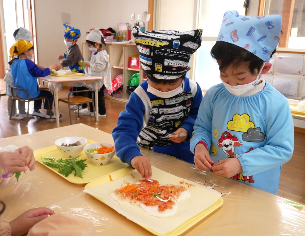 つぶしたご飯はグループのみんなの分を合体して、大きな1枚に♪
ケチャップでおいしい味付けをします。
「いいにお~い!」
「早く食べたいねぇ」
と、鼻に伝わる匂いから食欲を刺激される子ども達♡
まんべんなくケチャップを塗って、土台が完成したら、次はトッピング!
水菜・エリンギ、まいたけなどの食材は、ちぎって細かくするところから・・・
「みずなちぎったら、プチプチって音がするね」
「エリンギはなかなかちぎれんよ」
「まいたけはすぐさける!」
と、食材の違いを指先で感じながらご飯の上に置いていきます♪