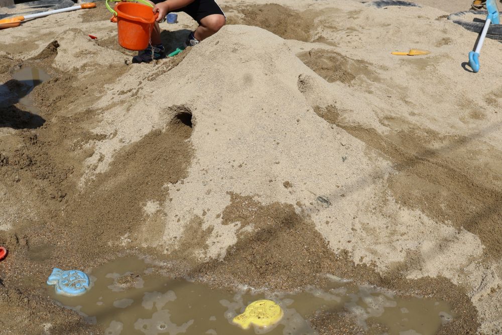 「今日も大きいお山作ろう!」
「ぼくはトンネル掘りたい!」
「水も流したいなぁ~」
と昨日の遊びから山作りを楽しみにしていた子どもたち。
山を作る人、トンネルを掘る人、水を流す人!
友達同士で“ここをもっとこうしよう!”
と話しながら、みんなで一つの大きな山を作りました。
Hくんがバケツで水を流し、
「海作ったよ!」
「お魚も泳いどるんよ!」 と!
イメージがどんどん膨らみます。