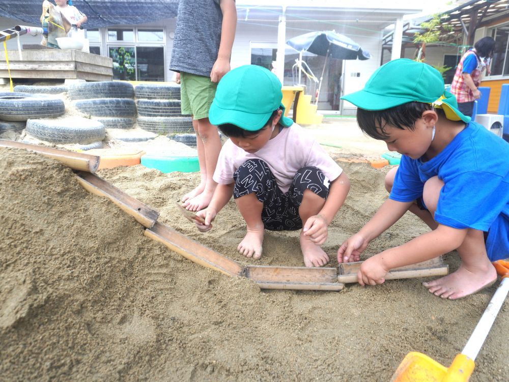 失敗をして… 考えて… やり直して…
繰り返しやってみることで気付くこと学ぶことがたくさんあります♡
さっそくトイを使ってみた!
竹を切ってくれたのは大坂先生!!
先生もみんなの遊びが楽しくなるように必要な時は協力します♡
「トイをつなげて水流したけど竹がずれた…」
「砂で横を埋めよう!」
「竹と竹を重ねたらいいかも!」
ウォータースライダーはどうなっているかイメージをし試行錯誤!