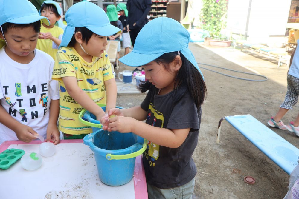 なんと中身は‼

手がいっぱいになるくらいの
まんまるの氷でした☆
 でも、
ただの氷じゃない…
なんと氷の中に恐竜や昆虫が…‼🐛

助け出そう！でもどうやって氷を溶かすのか
「水につけたらいんじゃない？」
そういってみんなバケツを準備♪

