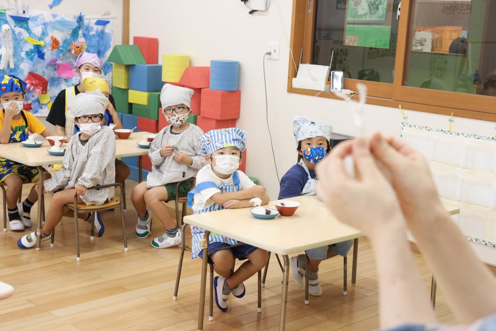4歳児ゾウ組、楽しみにしていたクッキングです
お彼岸ということで「おはぎ」を作りたいと思います
まずは本田先生がお手本を披露します
もち米入りのご飯を軽くつぶして平らにしていきます