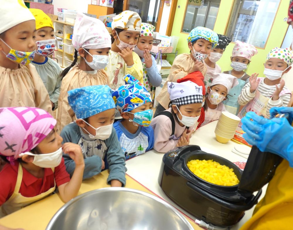 キリン組さんが園庭で育てたさつまいも＆お米(ちょびっとの玄米)を、新米(白米)と一緒に炊いて、さつまいもご飯に変身です♡

朝からキリン組の保育室で準備して炊いていた“さつまいもご飯”。
保育室の中はすでに良い匂いがしています。
では、炊きたてご飯を見てみましょう♡

ぱかっと蓋を開けると、一気に湯気が立ち上ります。
「わぁ～、あつそう！」
「焼き芋みたいないい匂い！」
大喜びの子ども達。

大きなボウルに出し、黒ごまを入れてしっかり混ぜます♪