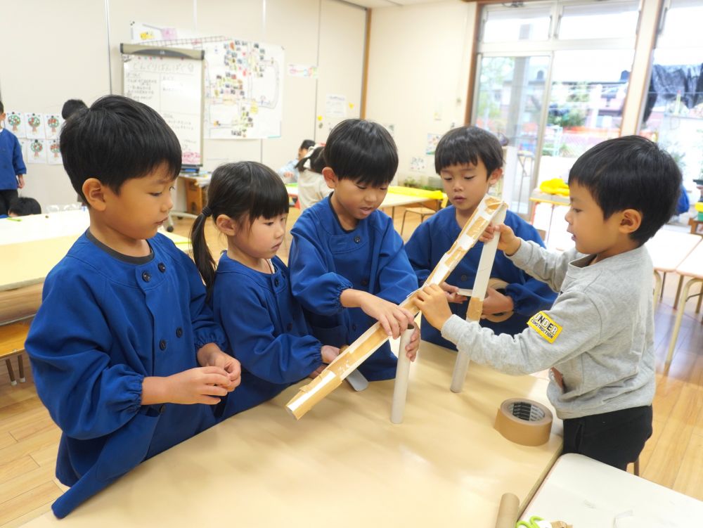 イメージがどんどん膨らんできて順調に進む『ピタゴラスイッチグループ』
道を作ったりつなげたりと役割分担をしながら進めています！
柔軟な発想とアイデアをそれぞれが出し合ってみんなで協力♡



「道は何で作る？」
「トイレットペーパーの芯をつなげよ！」
「つなげたら貸して！道を長くするわ！」
「ここ支えとくね！」
「立てるのはラップの芯を使おう！」
意見の共有と役割分担がスムーズにできています！