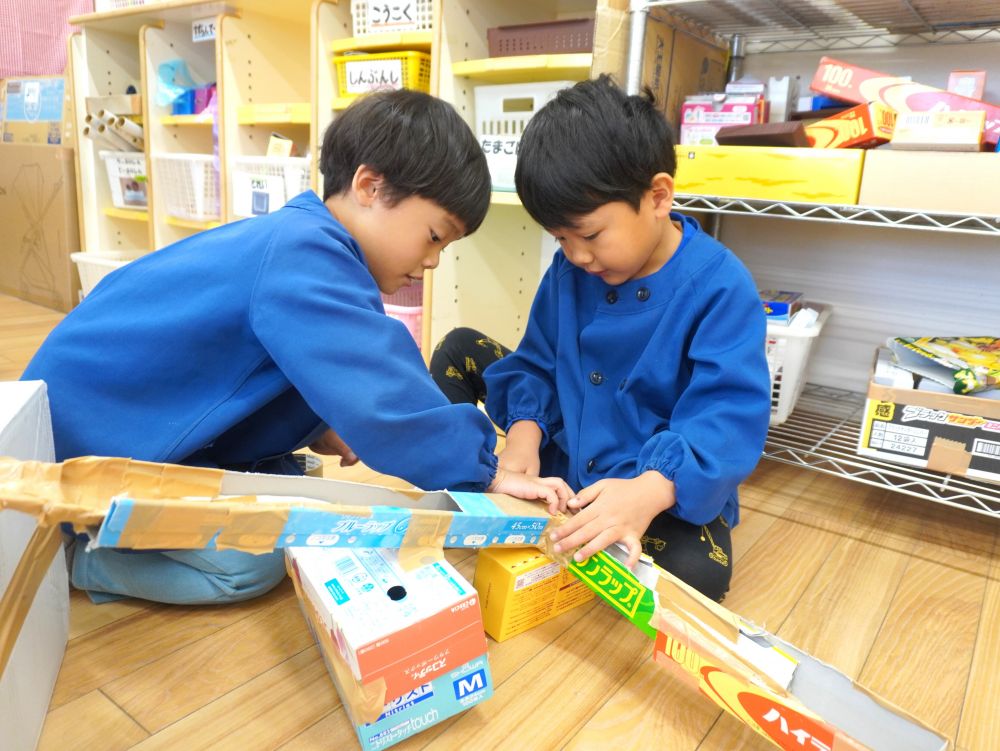 「カーブの道を作りたいね」
「カーブはこうやったらできるよ」
箱を切ってつなげてパパッとカーブを作ったSくん！
坂道になるように廃材を使って高さも調整します！