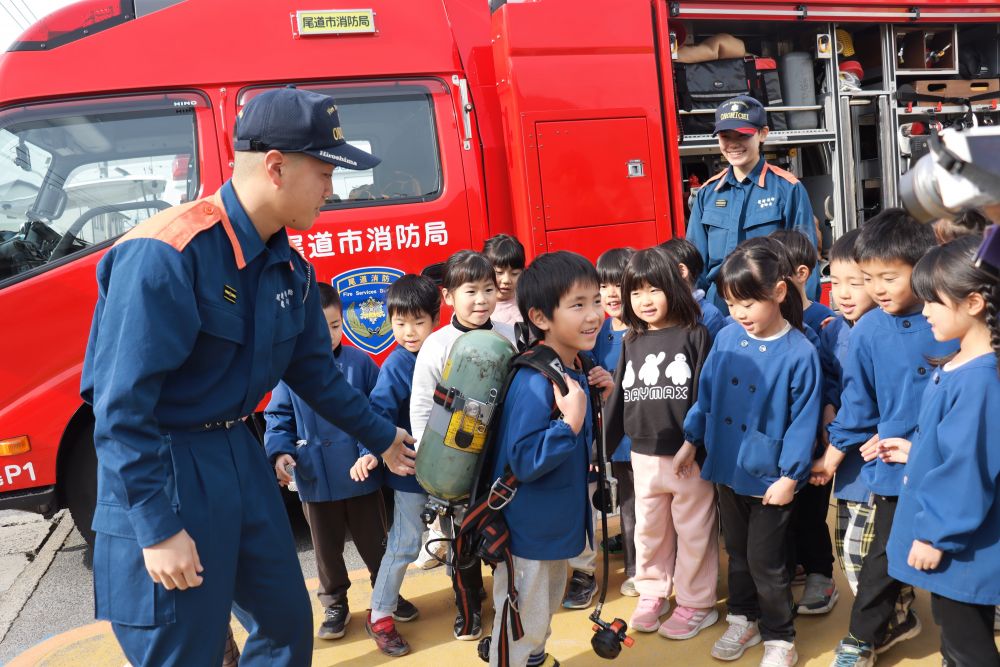 消防車や救急車には様々な道具が積んであります
「あれは何～？」「これは何～？」
子ども達の質問に笑顔で答えてくれる消防士さんです

今回はこんなサービスまで！
約１０キロある酸素ボンベを背負わせてもらいました
「これを背負って火を消したり人を助けたりするんだって」
「消防士さんってすごいね！」