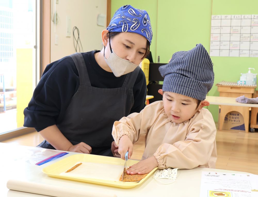 生地が薄く延びたら、次はカットする作業。
包丁やスケッパーを使い、細く切ることができるかな？？

難しいときにはおうちの人にも手伝ってもらい、ゆっくり切っていきます。
細く切るとカリカリ食感に、太く切るとサクサク食感に。
どんな風に切っても大丈夫♪手作りならではのおいしさが楽しめます♡

包丁を持つ子ども達より、おうちの人の方が緊張しているようで・・・。
楽しそうに包丁で切るRくんの横で、手がグーになり、力が入っている様子のお母さん。
心配そうに、でも手を出さず優しく見守る姿に大きな愛を感じます♡