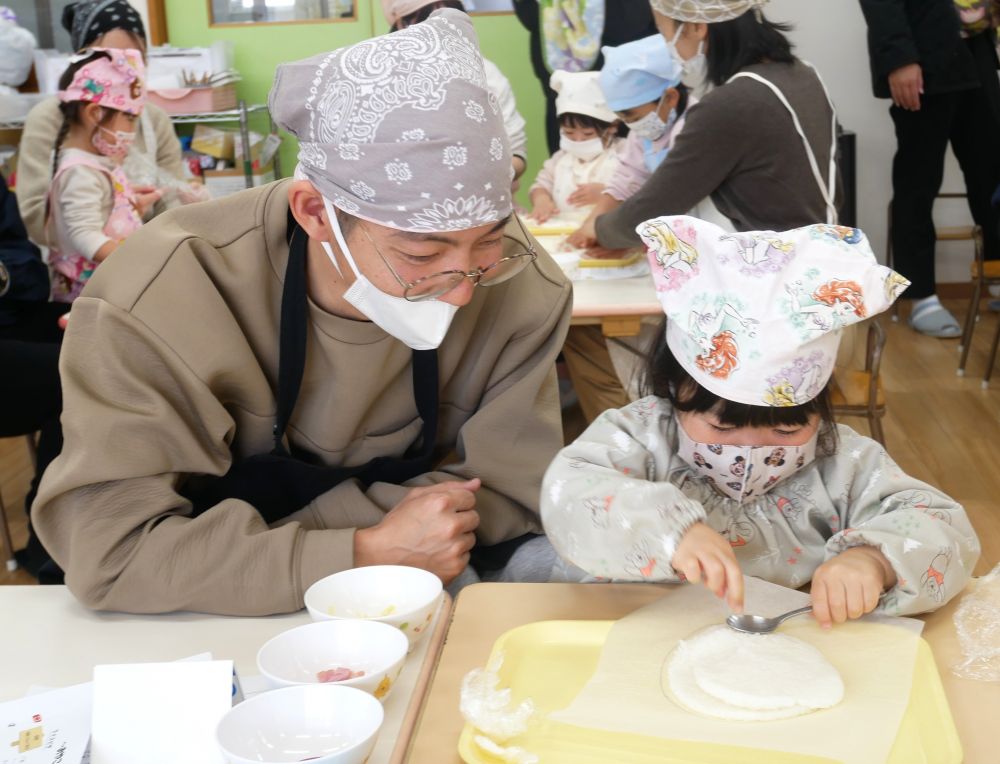 まず最初に、ご飯を使ってピザの土台作りから。
ラップに包んであるご飯を、指でつぶしていきます。

「むにゅむにゅしておもしろいねぇ」
「ラップが破れんようにせんとね！」
と、気づいたことを親子で伝え合います。

「もういいかなぁ？」
「ここ、もうちょっとつぶしとく？」
と、相談しながら作っている姿が微笑ましい♡