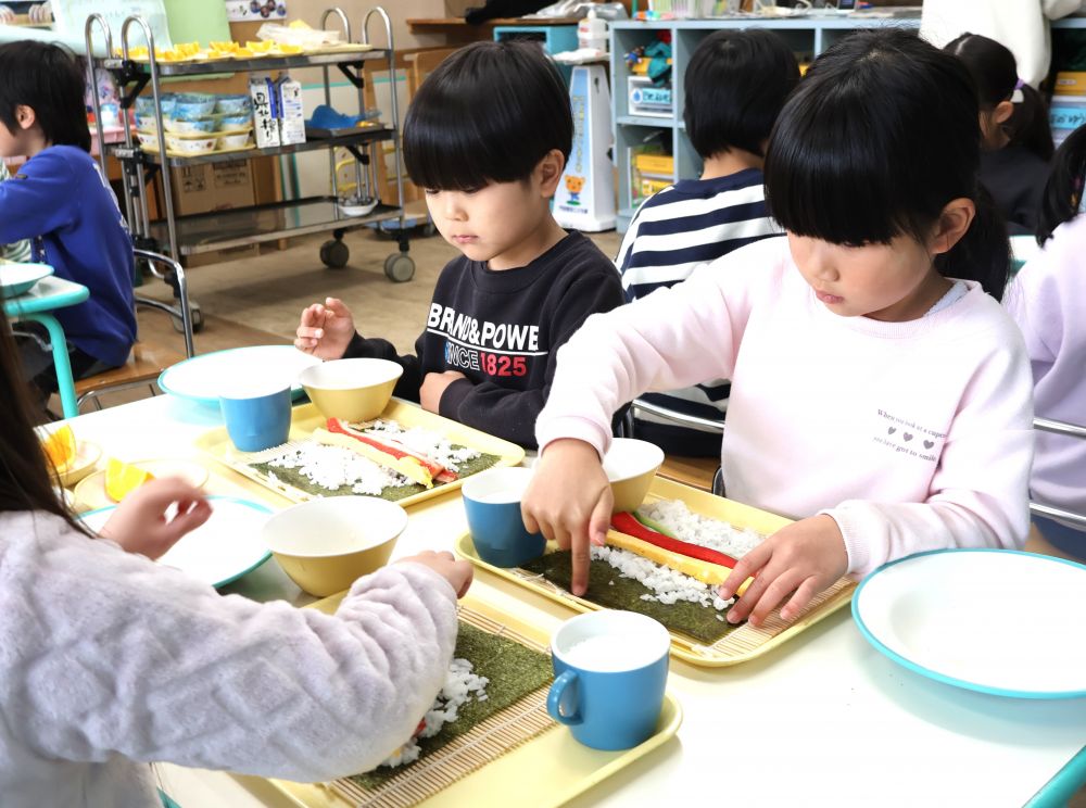 「鬼は外」　「福は内」で、おなじみの今日は2月３日『節分の日』です
【一年間健康に過ごせるように】という願いを込めて「悪いもの」を追い出す行事とされています

園でも豆まきなどの節分行事を楽しみ、給食も【恵方巻】と【いわしのつみれスープ】を食べました。

キリン組さんは自分で【恵方巻】に挑戦！！
給食先生が
巻きすに海苔をのせて・・・　海苔はざらざらが上だよー

「まきすってなに～」
「ザラザラって音が鳴る方よー触ってみー」
「なんかたのしー」