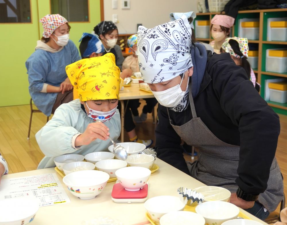 3歳児・4歳児さんの親子クッキングとは少し違い、5歳児さんは材料や道具を準備するところから自分たちで♡
まずはグループごとの材料等を取りに行き、自分たちの机まで持ち帰ります。

工程表を見ながら、何がいるのか・・・何個いるのか・・・
友達と分担して取りに行きます。
「小さいお皿が20枚いるんだって！」
「1，2，3，4，5，6，7，8，9，10，11，12，13，・・・あれ、わからなくなっちゃった・・」
10を超える数はまだまだ難しい・・さぁ、どうしよう？？友達と考えます・・・。
「じゃあ、10個で一回置いてくる？」「そっか、じゃあもう一回来るね！」
なんて良いアイデアなんでしょう！
困ったら、相談して、考える。自分たちで解決策を見いだす力やその姿に、成長を感じます♡

