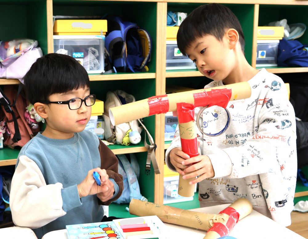 自分たちが作っている物をお店屋さんに出せる喜びを感じながら準備中★
「次は何がいる？」
「武器じゃない！？」
「ボールをバーンって打つ（鉄砲）武器がいいな！」

鉄砲のような形で持ちやすくしたいと考えたYくんとTくん
そのためには、どんな廃材を使おうかな
廃材コーナーの前で相談したり・・・
自分で今まで作ってきた武器を振り返ったり・・・
そして
「トイレットペーパーの芯をつなげよう！」
「いいね～やってみよう」

はがれにくく壊れにくい布ガムテープを選び芯を繋げて
鉄砲を長くしたり・・・持つところを作ったり・・・
さらにボールを入れは、ボールがしっかり入る大きさのトレイを鉄砲につけ完成☆
お客さんが持ちやすいよう工夫！！
想像しているものを友達と表現することを楽しみました♪