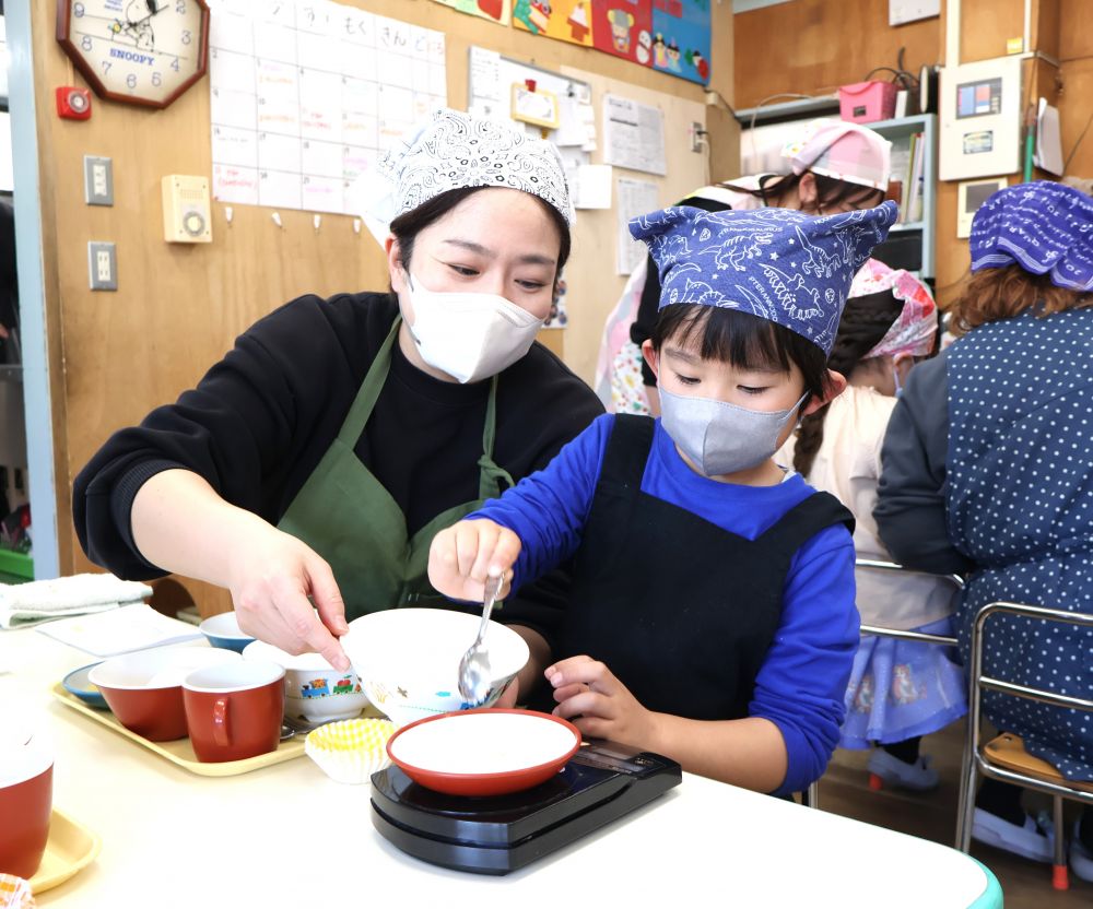 おうちの人と一緒にレシピを見ながらクッキングスタートです♪

まず、マドレーヌのホットケーキ粉と砂糖を計量器で測ります。

「どのくらい？？」
「あと５たして～」
「あっ　多すぎたー・・・どうしようー」
「少し取ればいいよ‼」

慎重にスプーンで粉をすくって減らします。
粉がこぼれてもご愛敬♡数字を見ながら親子の会話も弾みます。

おうちの人も
　…今日はゆったりとした気持ちで子どもと向き合いましょう…
にこにこ笑顔で子どもたちを見守ります♡
