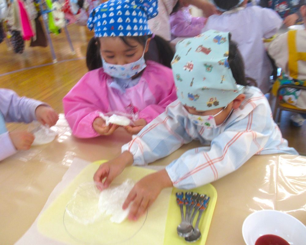 まずは、土台となる生地作りから。
ラップに包んだご飯をつぶして、もちもち食感が出るようにします♪
指でもみもみしたり、上から押したり、どうしたら上手くつぶせるか、自分たちで考えます。

「上を持っとかんと、ご飯がはみでるんよ」
「ご飯つぶすの楽しいねぇ～」
と、気づいたことや感じたことを伝え合います。

「ぺったんこになったよ～！」と、見せてくれたRくん。
もちもちした生地になりそうだね♡