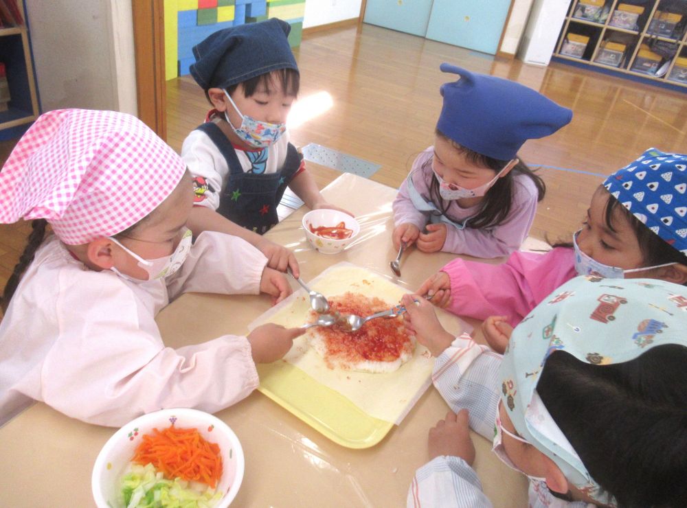 つぶしたご飯はグループのみんなの分を合体して、大きな１枚に♪
ケチャップでおいしい味付けをします。
「いいにお～い！」
「もうおいしそうよね♪」
と、鼻に伝わる匂いから食欲を刺激される子ども達♡
まんべんなくケチャップを塗って、土台が完成したら、次はトッピング！
