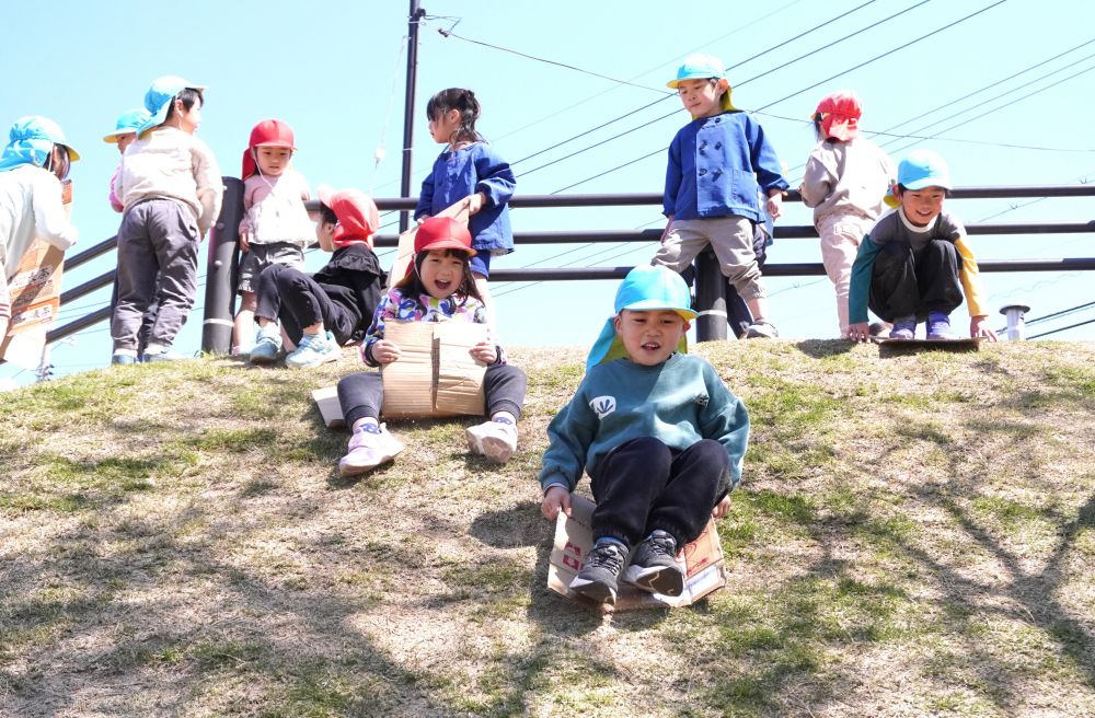 さっそく芝滑りスタート！
「段ボール貸して？」
「いいよ一緒に滑ろう！」
「わぁ～おしりが痛い！」
「２人で乗ってみよう！」
キリン組さんからやり方を教えてもらいながら
ゾウ組さんもチャレンジ！



