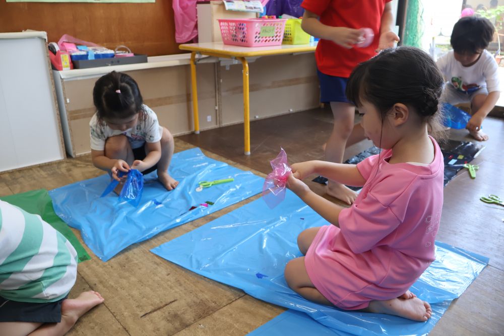 「雨の日でも外で遊べたらいいのに～」

そんなつぶやきも聞こえていたゾウ組さん。
だったら遊べる準備をしてみよう！と、自分たちでカッパを作りました。

何で作れるかな？
新聞紙ならおおきいかな？
折り紙もかわいいけど、どっちも濡れちゃうね
ビニールだったら大丈夫！
キラキラテープでかっこよくしたい！

どんな素材が使えるかみんなでアイデアを出し合って作り始めました！
