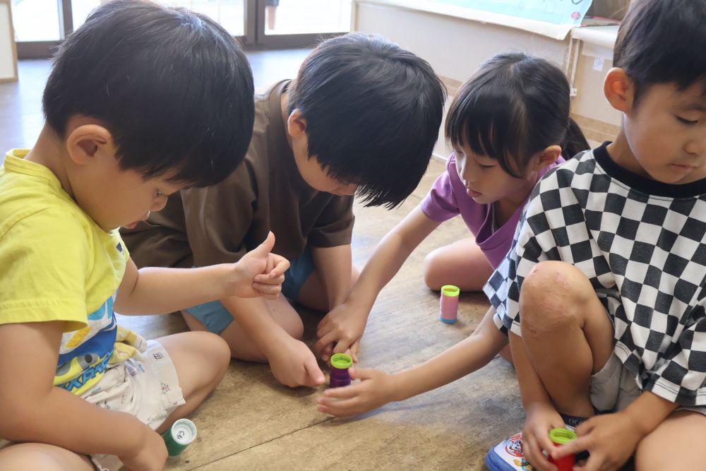 ペットボトルのキャップで作ったコマの
コマ回しに挑戦✨
まわすにはコツが必要！


Mくん「どうやってまわすの？」
Hちゃん「いちと、グーの指を作って・・・」

回せるようになった友達同士で教え合い！
何度も挑戦して回せるようになってくると、

Aくん「せんせい！Mくん回せるようになったよ！」
Kくん「見てあげて！」

と、自分のことのように声をかけてくれます